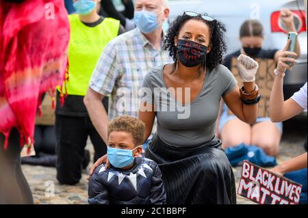 Richmond, North Yorkshire, UK - June 14, 2020: A woman wears a Black Lives Matter PPE Face Mask and salutes while holding her son at a BLM protest in Stock Photo