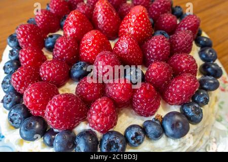 A cake decorated with butter icing and summer fruits including strawberries, raspberries and blueberries. Stock Photo