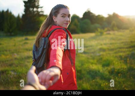 Young woman with backpack in summer nature, looking over shoulder at man. Stock Photo