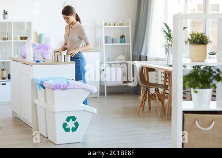 Young woman standing at the kitchen table and recycling plastic bottles and can Stock Photo