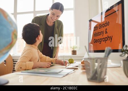 Portrait of smiling young mother helping little boy studying online at home, copy space Stock Photo