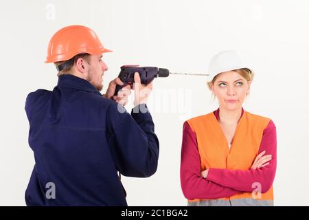 Woman with bored face in helmet ignoring husband annoying her. Marriage issues concept. Man with drill tool drills head of woman, white background. Builder, repairman makes hole in female head. Stock Photo