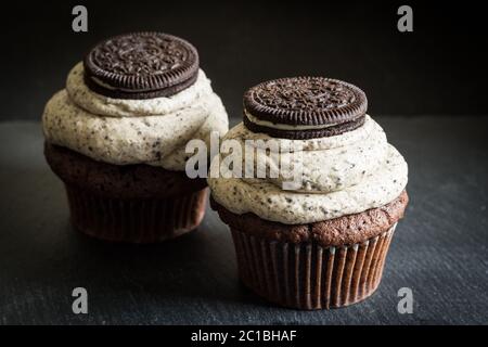 Two dark chocolate biscuit decorated chocolate sponge cup cakes close up on black background Stock Photo