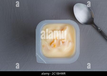 Healthy peach fruit flavored yoghurt with natural coloring in plastic cup isolated on gray texture b Stock Photo