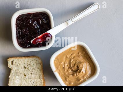 Peanut butter and jelly in bowls with knife and slice of bread on grey background with space for tex Stock Photo