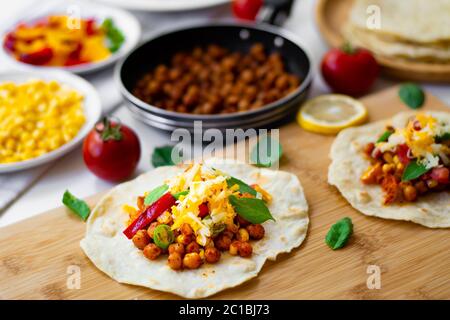 Vegan tortilla tacos with chickpeas, bell peppers, corn, tomatoes, basil leaves and green chili. On the background are ingredients, lemons, chickpeas Stock Photo