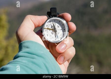 Close-up A man's hand holds a pocket compass against the backdrop of mountains and woods. The concept of outdoor navigation Stock Photo