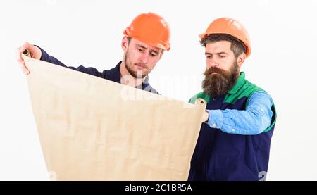 Builder, engineer, architect work at site. Men in helmets with blueprint on white background. Architect and build concept. Architects in hard hat on busy faces looks at drawing, plan, project. Stock Photo