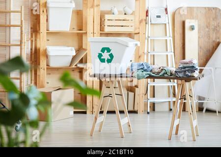 Image of table with plastic trash container and heap of clothes on it in the storage room Stock Photo