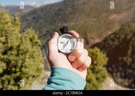 Close-up A man's hand holds a pocket compass against the backdrop of mountains and woods. The concept of outdoor navigation Stock Photo
