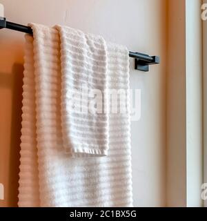 Square White towel hanging on black rod mounted on the bathroom wall with tiles Stock Photo