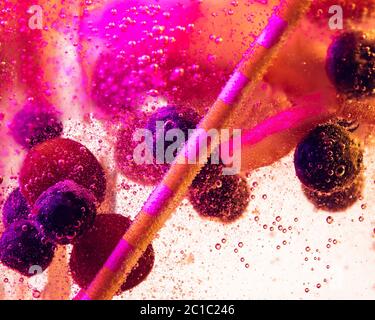 Close up view of the cold and fresh lemonade with bright berries and ice cubes in neon light. Texture of cooling summer's drink with macro bubbles on glass. Fizzing or floating up to top of surface. Stock Photo