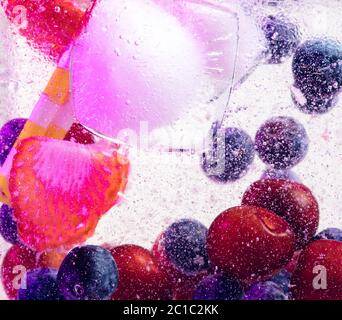 Close up view of the cold and fresh lemonade with bright berries and ice cubes in neon light. Texture of cooling summer's drink with macro bubbles on glass. Fizzing or floating up to top of surface. Stock Photo
