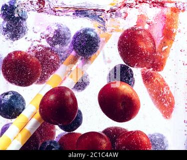 Close up view of the cold and fresh lemonade with bright berries and ice cubes in neon light. Texture of cooling summer's drink with macro bubbles on glass. Fizzing or floating up to top of surface. Stock Photo