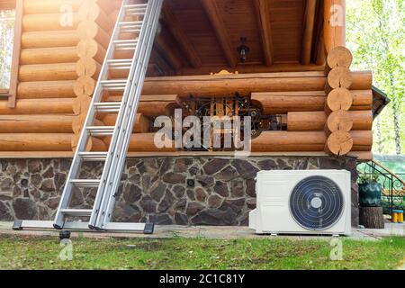 New modern HVAC air conditioning external compressor unit preapred for installation or replacement near wall of wooden log residential country cottage Stock Photo