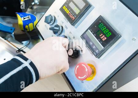 A close-up of a man's hand holds a rotary switch on the equipment control panel with instruments. Stock Photo