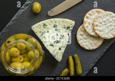 Cheese board with blue mold cheese, olives, pickles and crackers on black slate - top view photo Stock Photo