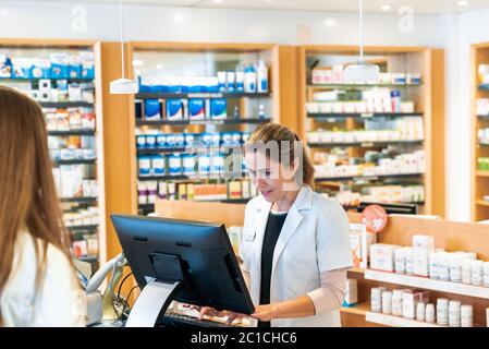 A blonde female pharmacist checks information on the computer for a customer in a pharmacy Stock Photo