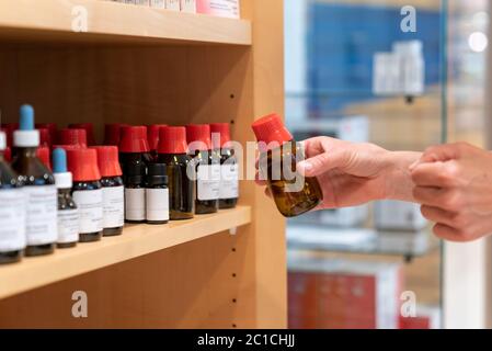 The hands of a female pharacist arranging normed brown glass apothecary bottles with sealed caps and droppers on a shelf Stock Photo