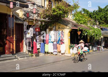 Clothes shop with local woman cycling past on street in old quarter of historic town. Hoi An, Quang Nam Province, Vietnam, Asia Stock Photo