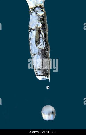 Nature's handiwork in winter. Macrophotography of icicle isolated on dark blue background showing tiny water droplets falling from melting tip. Stock Photo