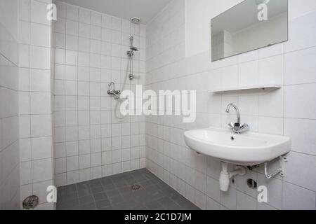 Simple, old clean bathroom with white tiled floor sink and shower Stock Photo