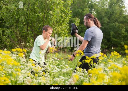 Father and son training to box in the park outdoors, fighting, care, sport, parenting, healthy lifestyle concept Stock Photo