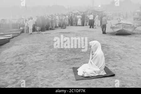 Solitary Hindu woman covered in shawl deep in mediation on bank of river Jamuna at dawn. Stock Photo