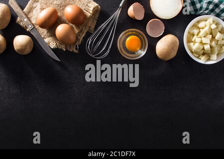 Spanish omelette tortilla ingredients: eggs, potatoes and onion on black slate background Stock Photo