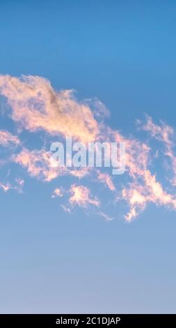 Vertical Wispy white clouds tinged pink at sunset Stock Photo