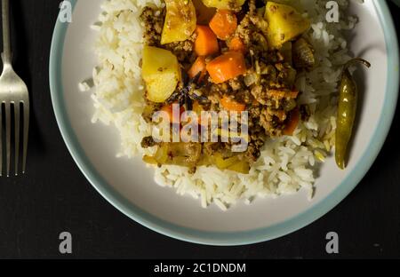 Curry beef mince carrots and rice in plate, top view photo on black rustic table Stock Photo