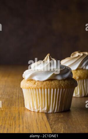 Cup cakes with white meringue frosting on wooden table, focus on front cupcake Stock Photo