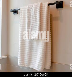Square Black rod with white towel mounted on the bathroom wall with tiles Stock Photo