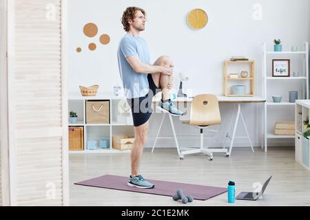 Young man standing on exercise mat and doing sports exercises in the room at home Stock Photo