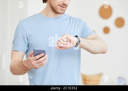 Close-up of young man looking at his watch and checking his time with mobile phone Stock Photo