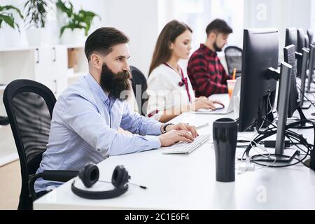 People working in modern IT office. Group of young and experienced programmers and software developers sitting at desks working on computers. Team at Stock Photo