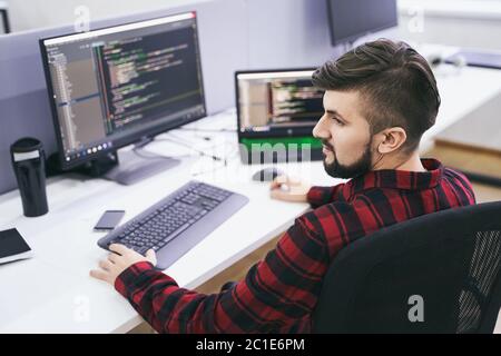 Software developer working on computer in IT office, sitting at desk and coding, working on a project in software development company or technology Stock Photo