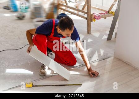 Master is wearing work clothes, is checking horizon of installing tiles, using building level, adjusting, professional repairing work Stock Photo