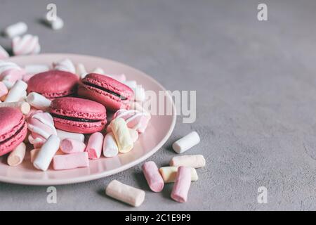 Tasty pink french macaroons and marshmallows on a plate. Grey background. Place for text. Stock Photo