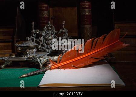 Retro quill pen and vintage inkwell on wooden desk in the old office against the background of the bookcase and the rays of light. Conceptual backgrou Stock Photo