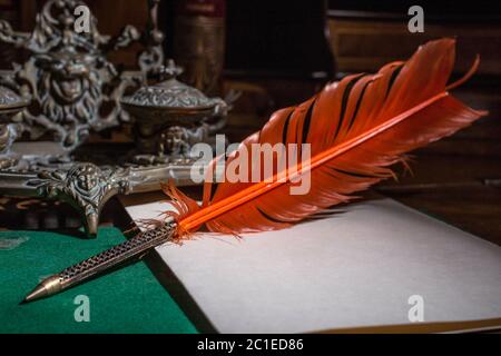 Retro quill pen and vintage inkwell on wooden desk in the old office against the background of the bookcase and the rays of light. Conceptual backgrou Stock Photo