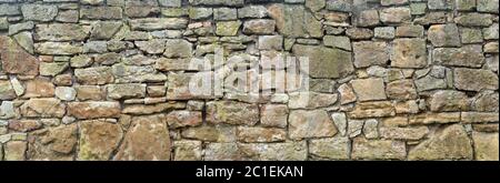 Panorama of a very old, coarse natural stone wall made of different sized stones Stock Photo