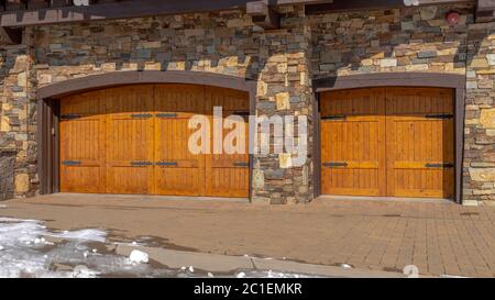 Panorama facade of home featuring two hinged wooden garage doors and stone brick wall Stock Photo