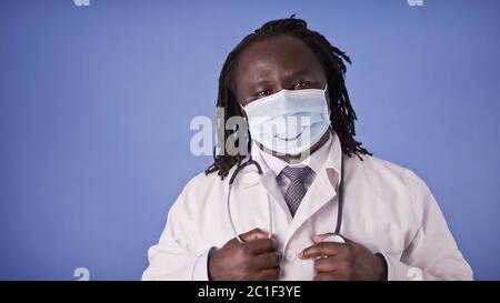 Portrait of an African Doctor in Face Mask with Smile on isolated on blue studio background. Stock Photo