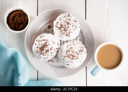 Cupcakes with whipped cream and chocolate chips on a white plate and a Cup of coffee in the background, on a white wooden table. Image for the menu or Stock Photo