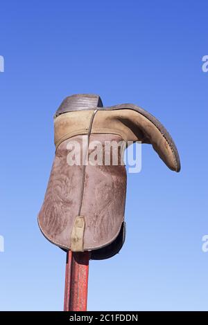 an old weathered cowboy boot on a metal fence post with blue sky background Stock Photo
