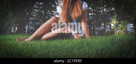 A young girl resting on the grass in the evening park, she rests her hands on the grass and maybe is going to lie down or get up Stock Photo