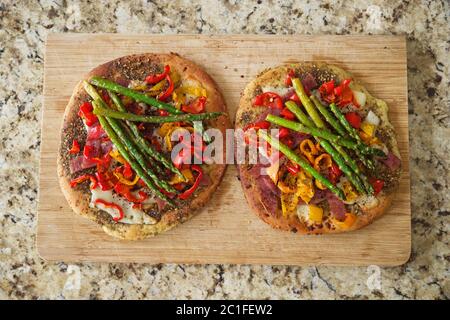two focaccia with peppers asparagus and salami on a cutting board Stock Photo