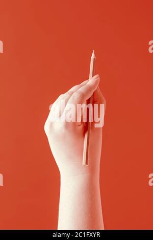 Left-hander woman's writing with a red pencil on a red-orange colored background. Woman's left hand with a pencil in duotone settings. Stock Photo