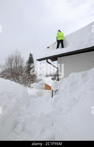A man shoveling high, heavy snow from a house roof Stock Photo